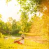 beautiful woman having rest under huge tree in sunset time outside. Sunset people. Lonely woman enjoying nature landscape in evening. Summer or spring day. Girl sitting on grass Color horizontal image